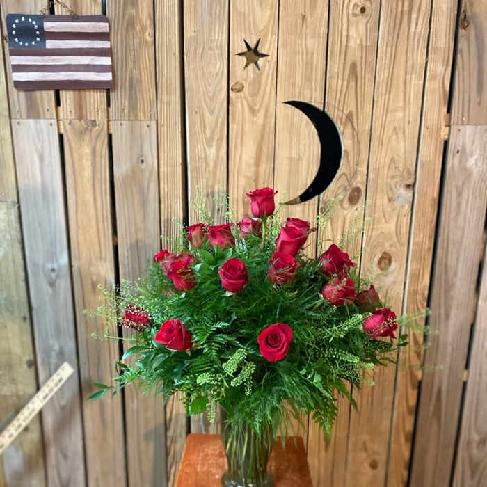 Red roses arranged in a glass vase with greenery