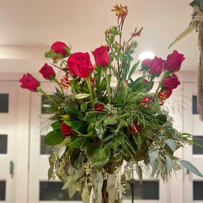 Tall vase arrangement of red roses with mixed greenery