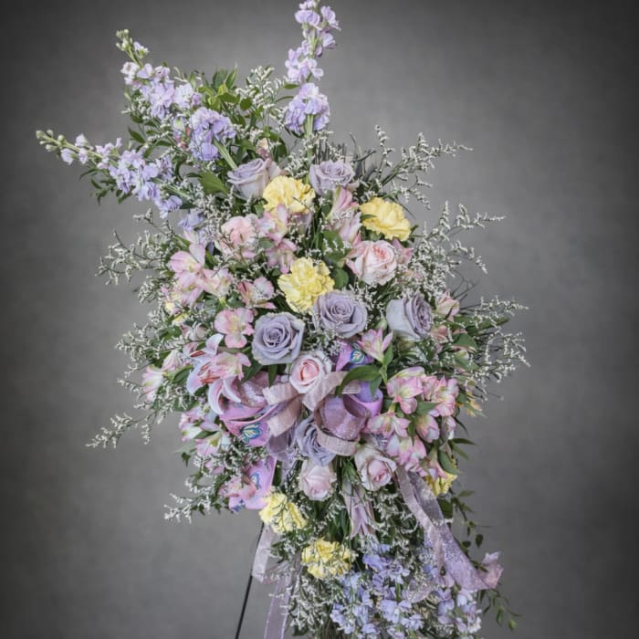 Large pastel floral standing spray with roses, lilies, and ribbons on an easel
