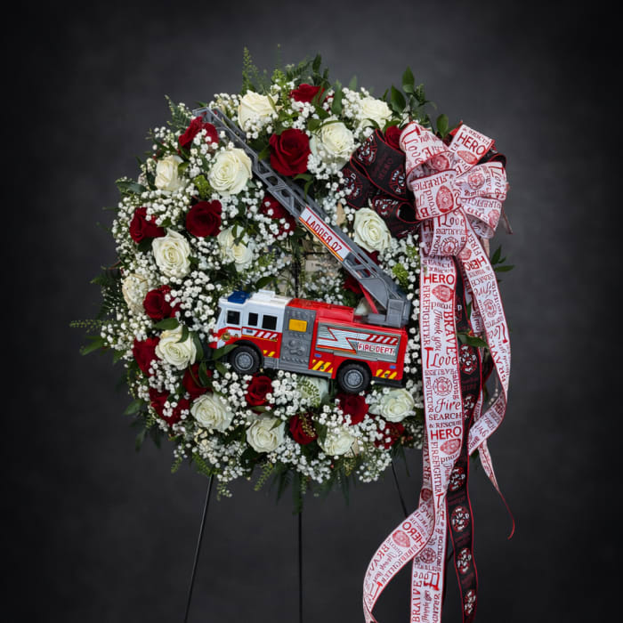 Firefighter-themed rose wreath with a toy fire truck and ribbon on a stand