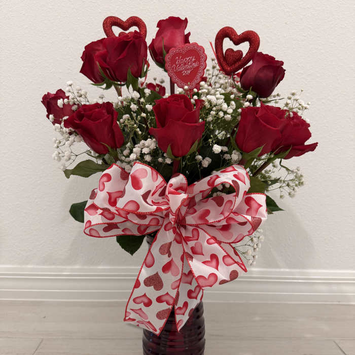 Red roses in a dark vase with a heart-patterned bow and Valentine topper