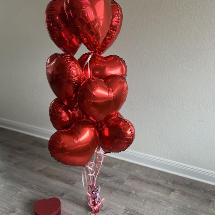 Cluster of red heart-shaped balloons with a small heart gift box on the floor