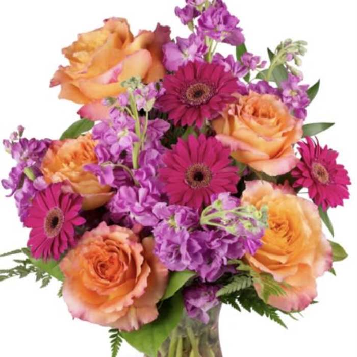 Orange roses and magenta gerbera daisies in a glass vase