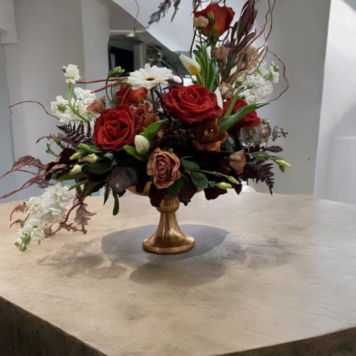 Red rose arrangement in a gold pedestal vase with white blooms