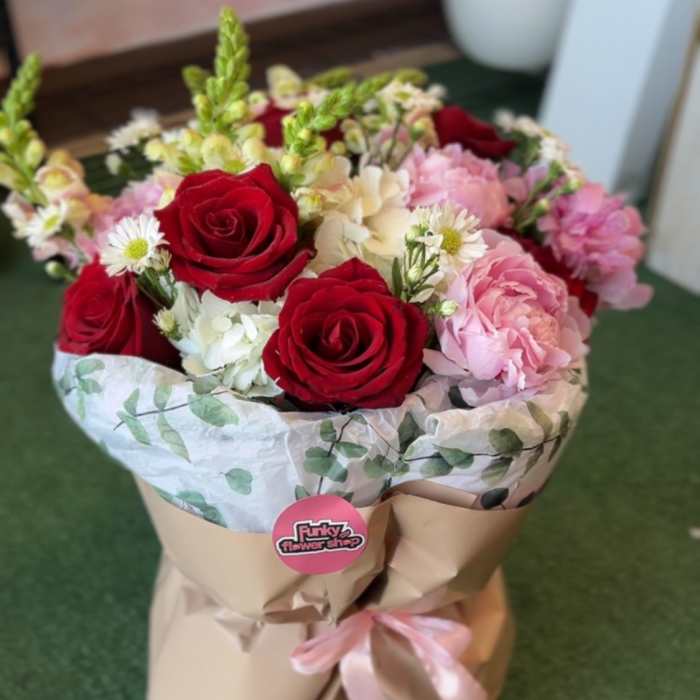 Bouquet of red and pink roses with white blooms in brown paper wrap