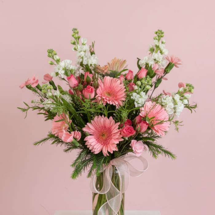 Pink mixed flower bouquet in a clear glass vase with a sheer ribbon
