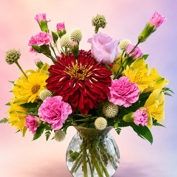 Mixed bouquet of red, pink, and yellow flowers in a clear glass vase