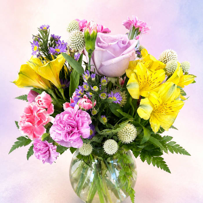 Mixed bouquet of pink, yellow, and purple flowers in a glass vase