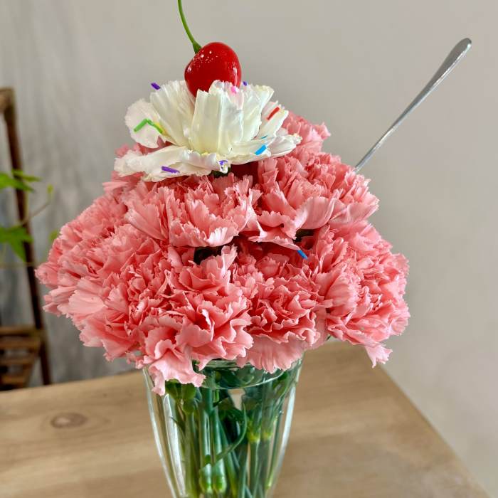 Pink carnations in a clear glass vase topped with a white flower and cherry