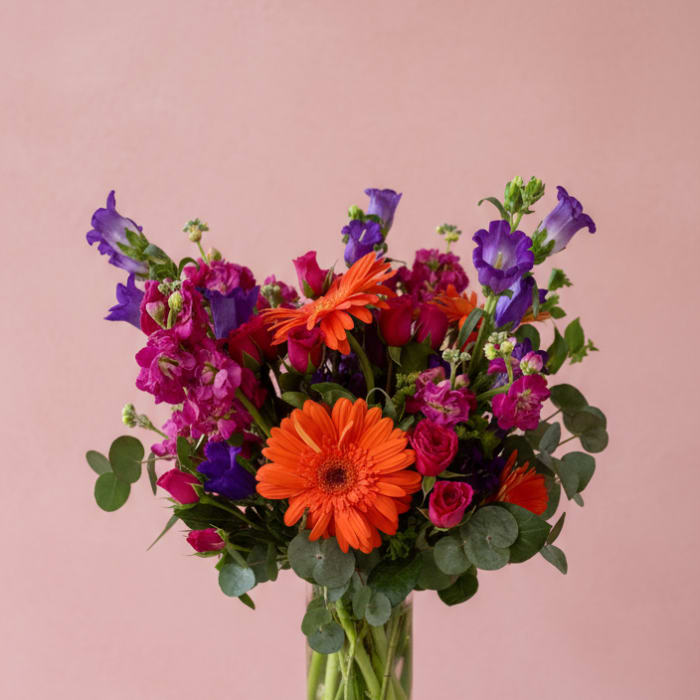Bright mixed bouquet in a clear glass vase with orange and purple flowers