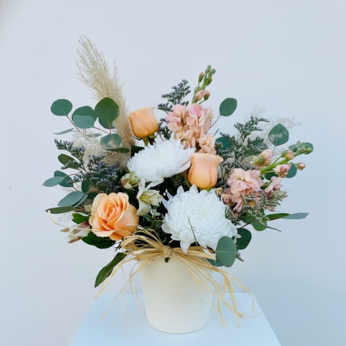Peach and white floral arrangement in a white vase with eucalyptus