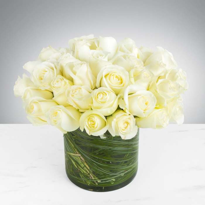White roses arranged in a clear glass vase with green stems visible inside