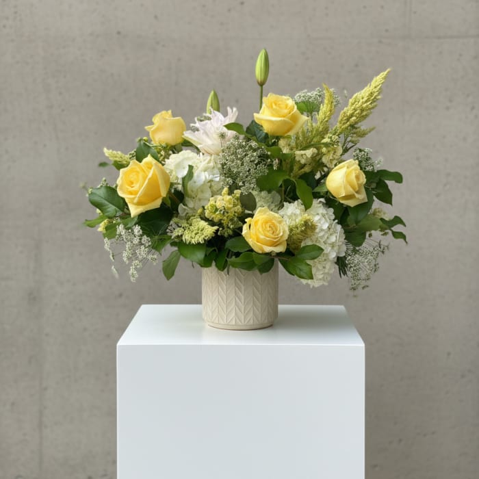 Yellow roses and white blooms arranged in a cream vase