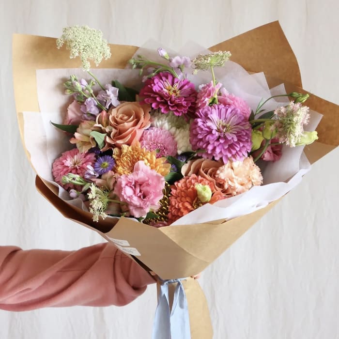 Hand-tied bouquet of pink, peach, and purple flowers wrapped in brown paper