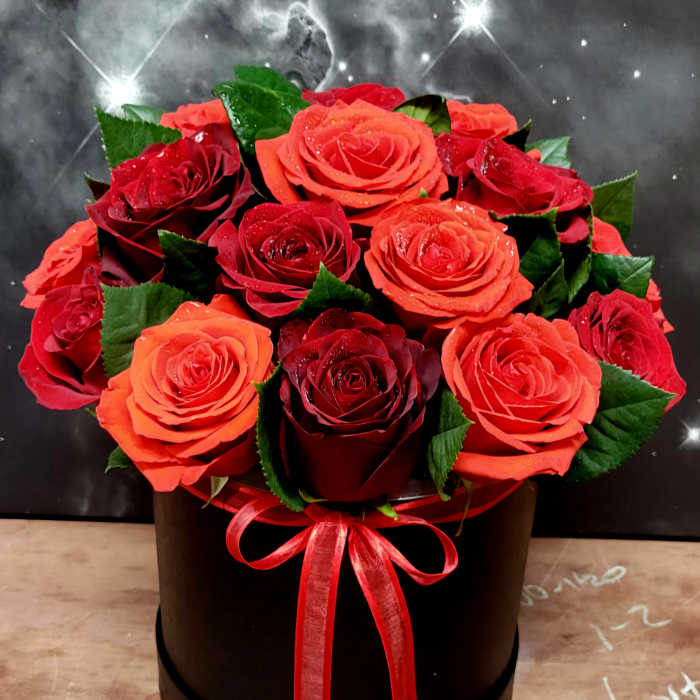 Red and orange roses arranged in a black round box with a red ribbon