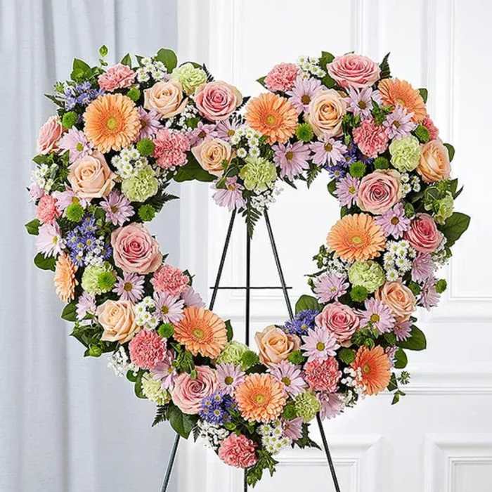 Heart-shaped floral wreath on a stand with pink, peach, and lavender blooms