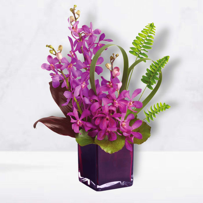 Purple orchid arrangement in a dark glass vase with green fern fronds