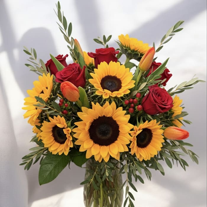 Bouquet of sunflowers, red roses, and orange tulips in a glass vase