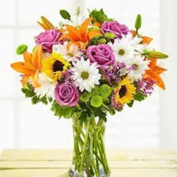 Mixed bouquet of orange lilies, purple roses, and white daisies in a glass vase