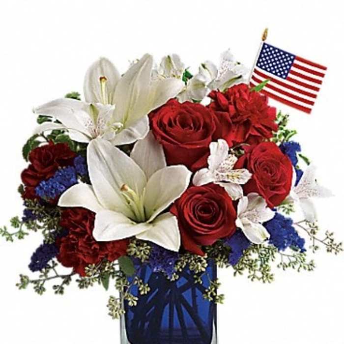 Red roses and white lilies in a blue glass vase with a small American flag