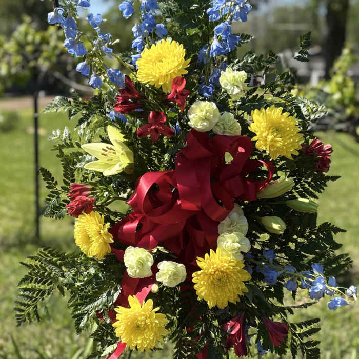 Standing floral spray with blue, yellow, red, and white flowers and a red ribbon