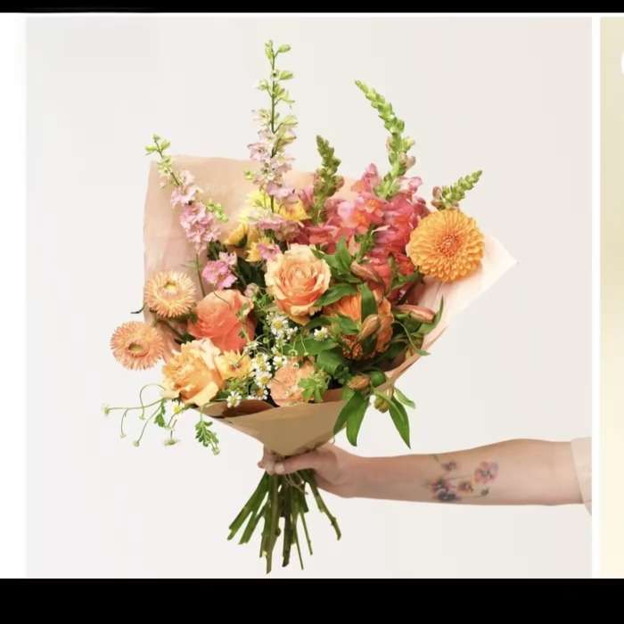 Handheld bouquet of peach, pink, and orange flowers wrapped in tan paper