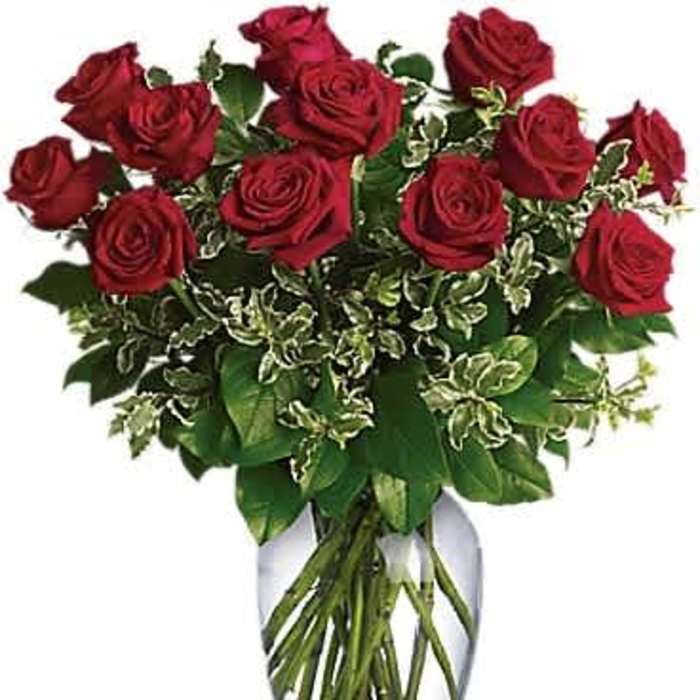 Arrangement of red roses with variegated foliage in a clear glass vase