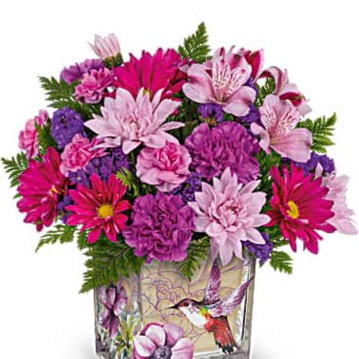 Bright pink and purple mixed flower arrangement in a square glass vase with a hummingbird illustration