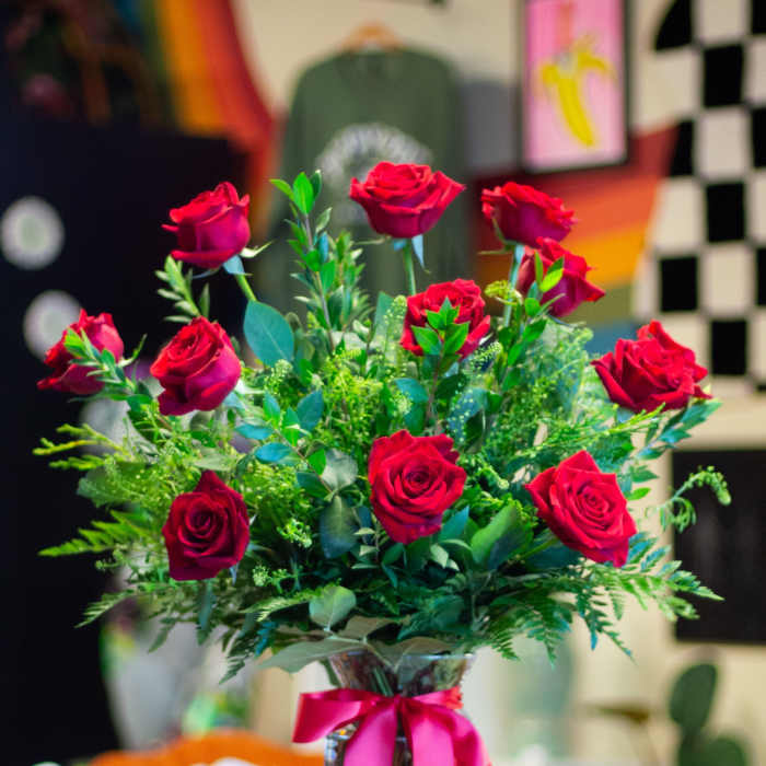 Red roses arranged in a clear glass vase with a pink ribbon