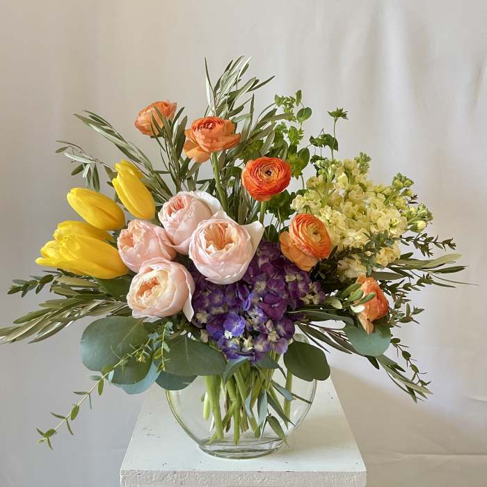 Mixed bouquet of yellow tulips, peach ranunculus, and purple hydrangea in a glass vase
