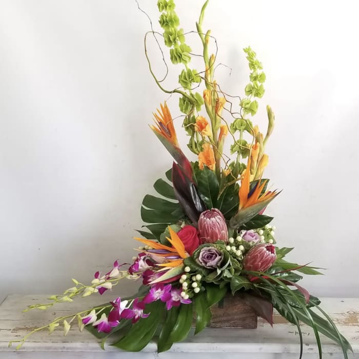 Tall tropical flower arrangement with orange bird-of-paradise and orchids in a wooden container