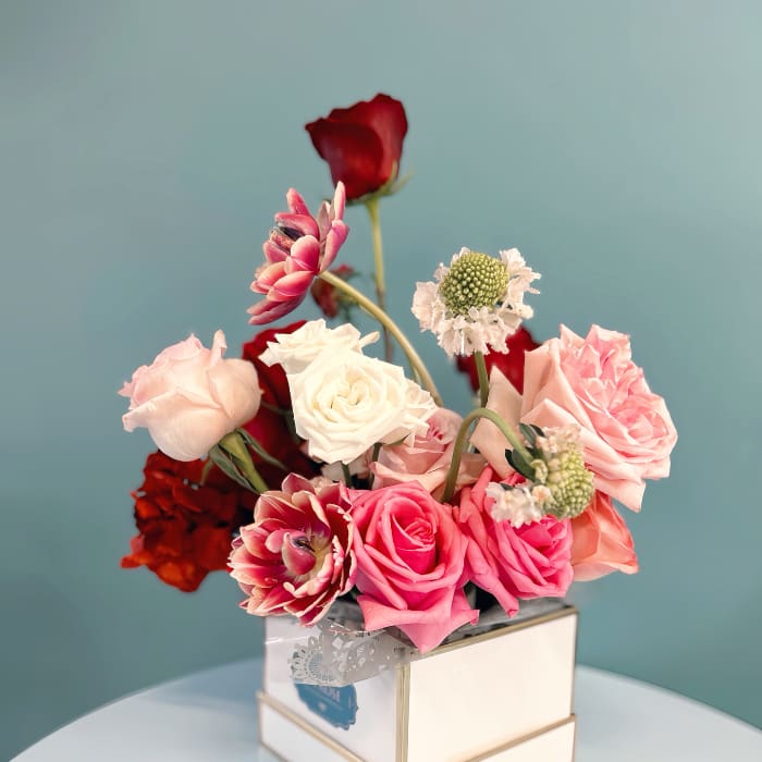 Pink and white roses arranged in a square box with a red rose accent