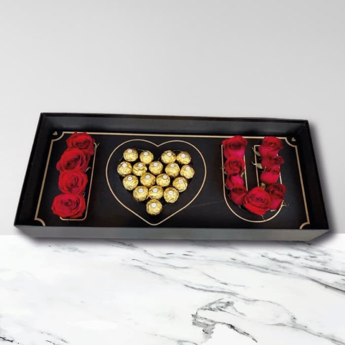 Black gift box with red roses and gold-wrapped chocolates arranged in a heart