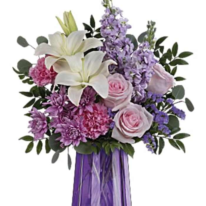 Mixed bouquet of white lilies, pink roses, and purple blooms in a faceted purple glass vase