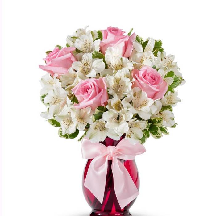 Pink roses and white flowers in a red glass vase with a pink ribbon