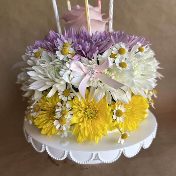 Flower-covered cake with candles and a pink rose topper