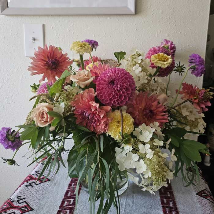 Loose garden-style arrangement of pink dahlias, roses, and white hydrangeas in a clear glass vase