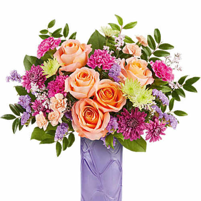 Peach roses and pink flowers in a purple glass vase