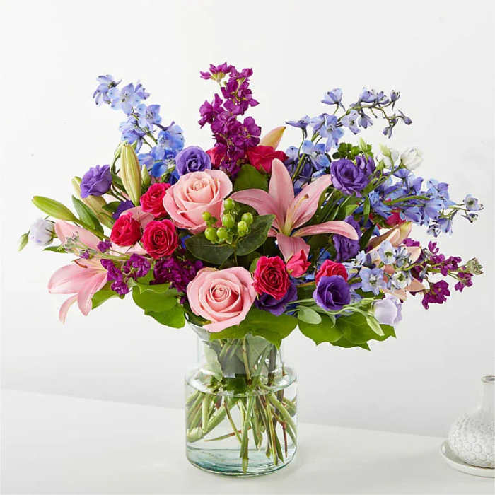Mixed bouquet of pink, purple, and blue flowers in a glass vase