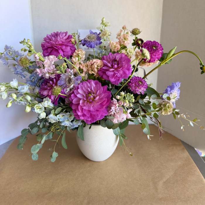 Mixed bouquet of purple, pink, and blue flowers in a white vase