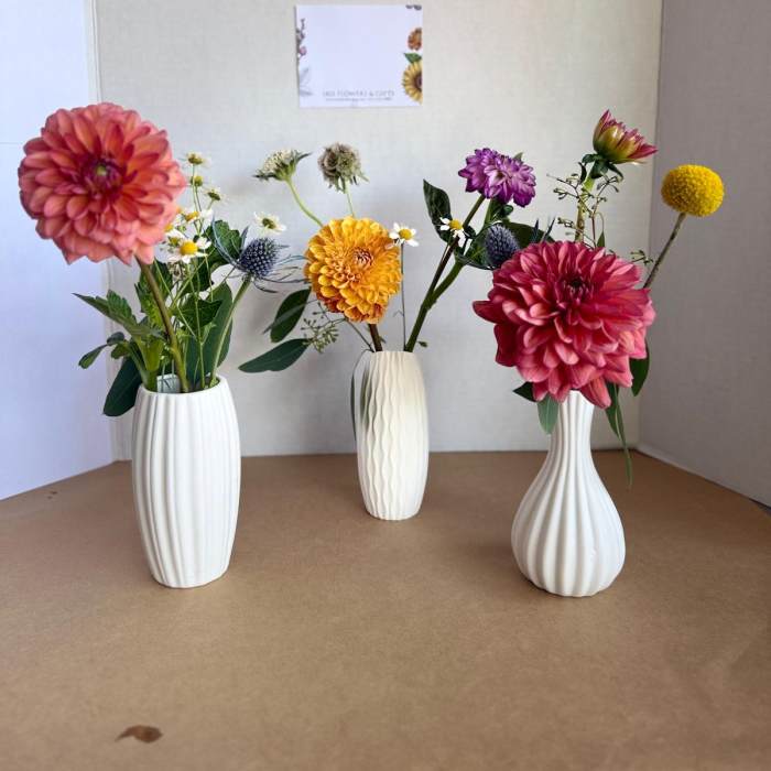 Three small floral arrangements in white vases with colorful blooms