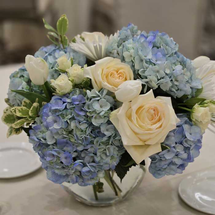 Blue hydrangeas and cream roses in a clear glass vase