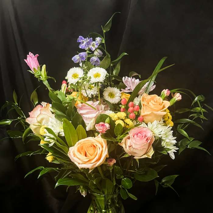 Mixed bouquet of roses, daisies, and purple flowers in a glass vase