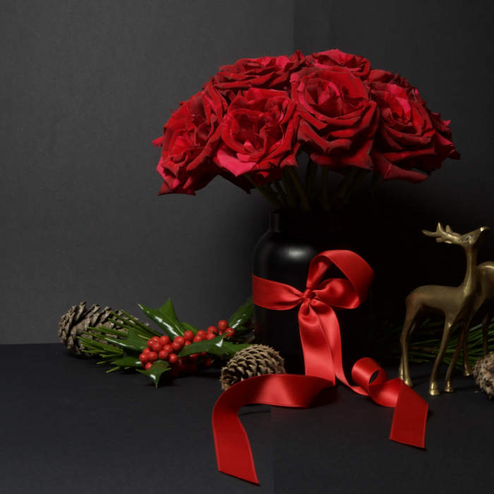 Red roses in a black vase with a red ribbon and holiday decor