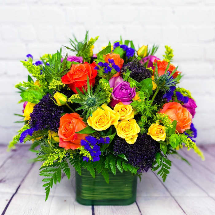 Colorful bouquet of roses and purple filler flowers in a green vase