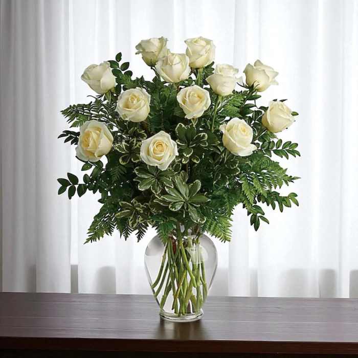 White roses arranged in a clear glass vase with greenery