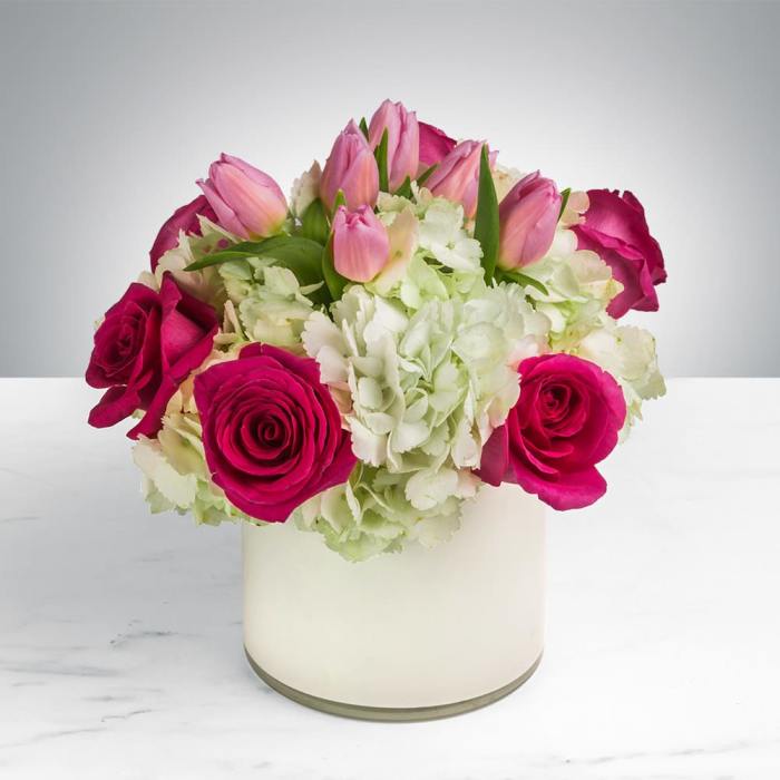 Pink tulips and magenta roses in a white vase with pale hydrangeas