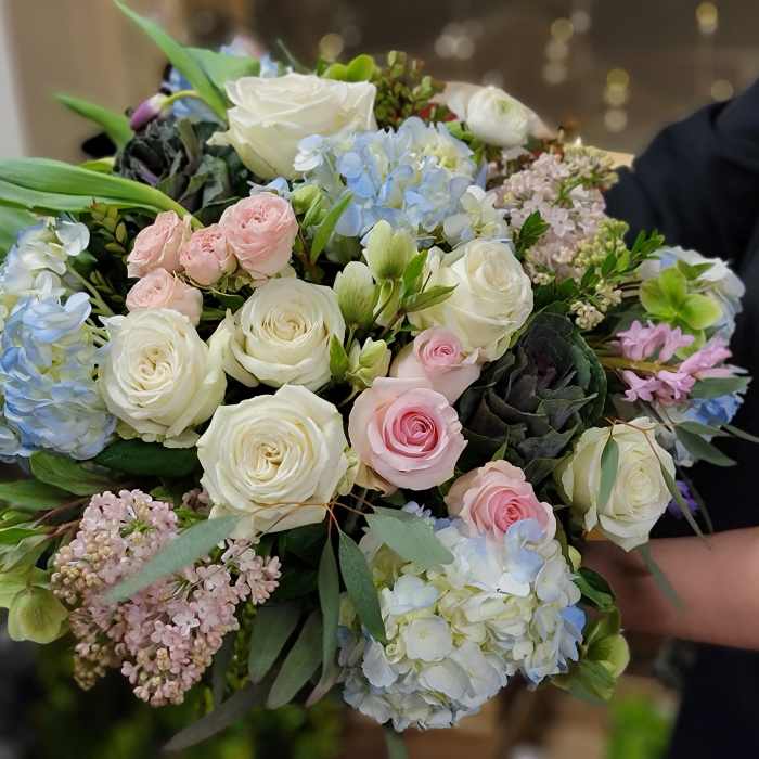 Handheld bouquet of white and pastel pink roses with blue hydrangeas
