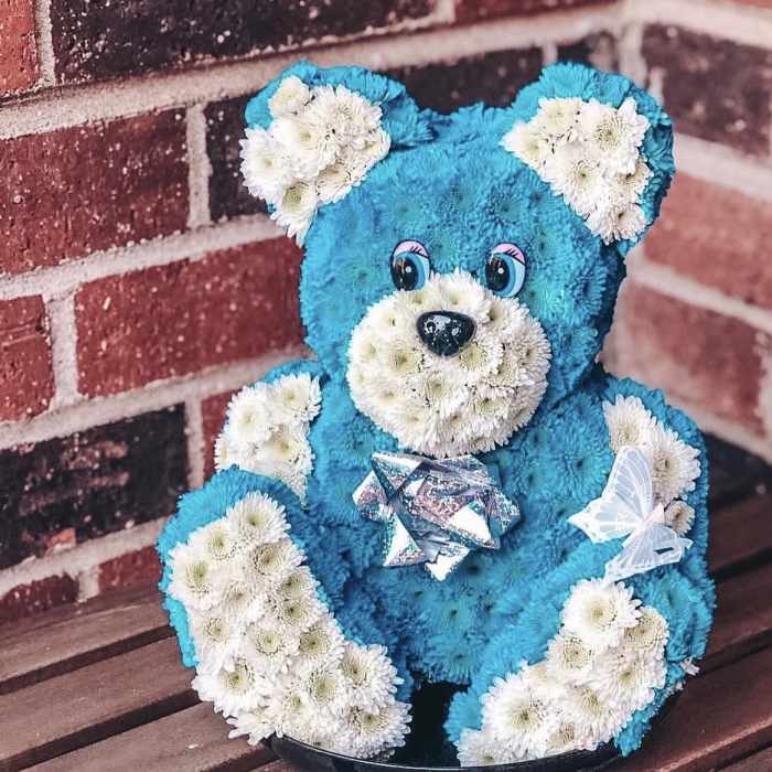 Blue teddy bear made of flowers with white flower accents and a silver bow