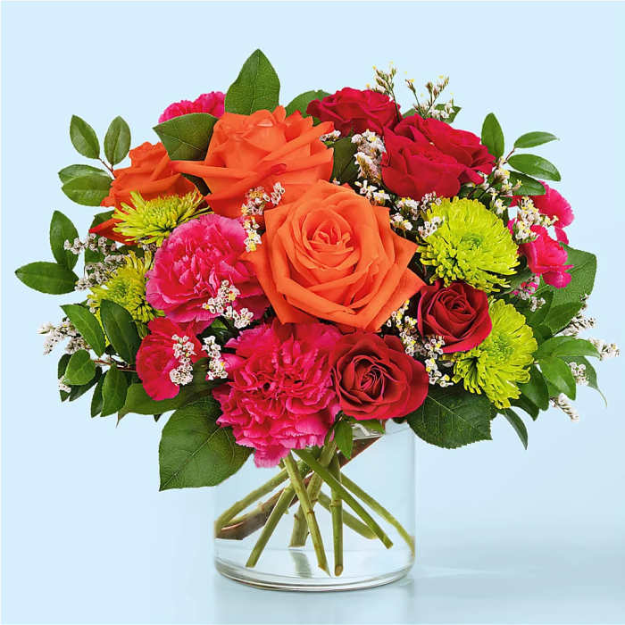 Mixed bouquet of orange, red, and pink flowers in a clear glass vase